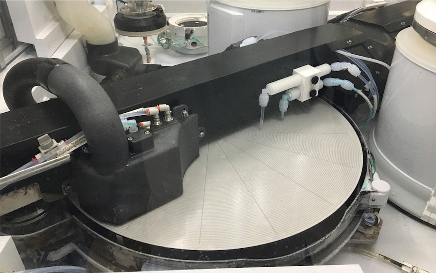 A slurry polishing machine in action, shaping a circular object with precision in a production environment.